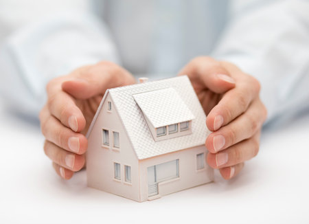 Property insurance. House miniature covered by hands.の写真素材