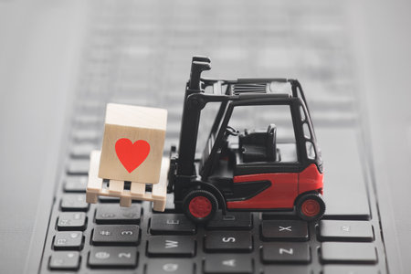 Forklift with red heart symbol on wooden block over laptop keyboardの写真素材