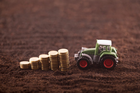 Tractor miniature with coins on fertile soil landの写真素材