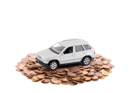 Small silver car on a pile of coins isolated on white backgroundの写真素材
