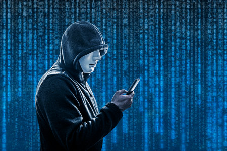 Hooded hacker with mask holding smartphone