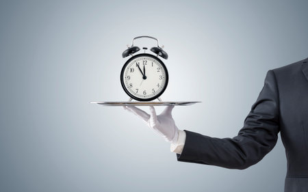 Businessman offering old style alarm clock on silver trayの写真素材