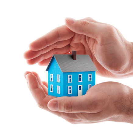 Small blue toy house protected by hands isolated on whiteの写真素材