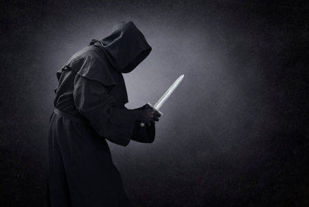 Hooded man with dagger in the darkの写真素材