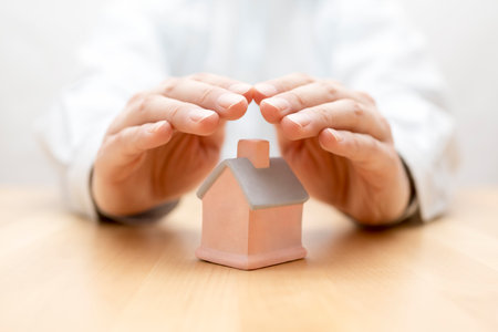 Property insurance. House miniature covered by handsの写真素材