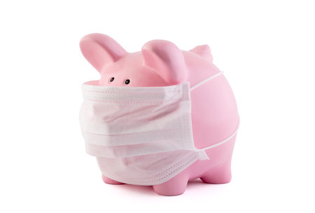 Pink piggy bank with protective medical mask isolated on white. Banking during a pandemic concept.の写真素材