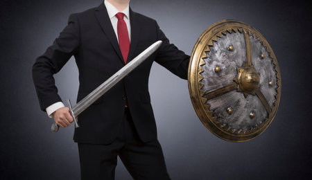 Businessman with sword and shield on dark background. Business protection concept.の写真素材