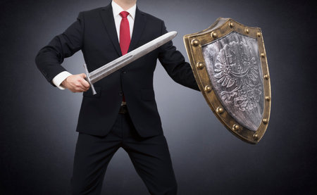Businessman with sword and shield on dark background. Business protection concept.の写真素材