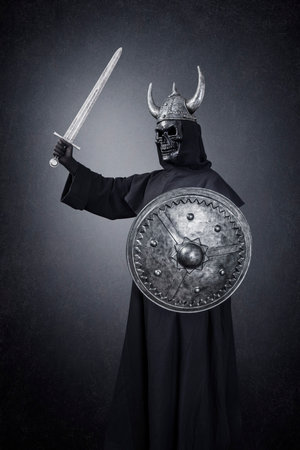 Skeleton warrior with horned helmet, sword and round shield in the darkの写真素材
