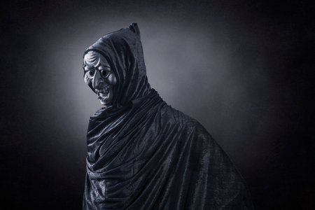 Spooky figure with hooded cape over dark misty backgroundの写真素材