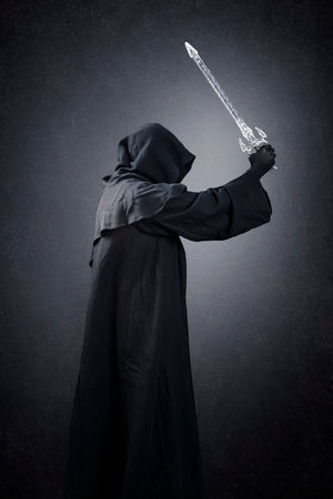 Dark knight with hooded cape and medieval sword over dark misty backgroundの写真素材