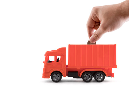 Putting coin into the red cargo delivery truck on white backgroundの写真素材