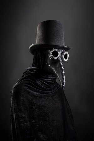 Plague doctor with black vintage top hat at night over dark misty backgroundの写真素材