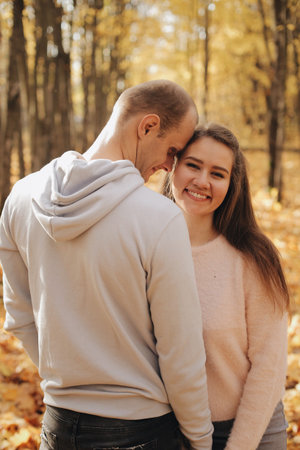 Couple stands in the forest together. Attractive girl hugging her boyfriend and looking at the camera. Happy family stay in autumn park.の写真素材