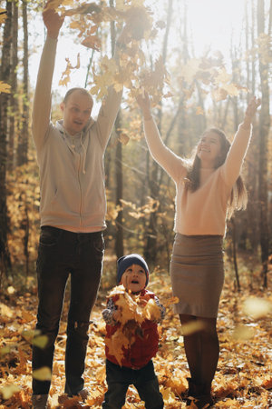 Happy family with son in autumn park throws yellow leaves.の写真素材
