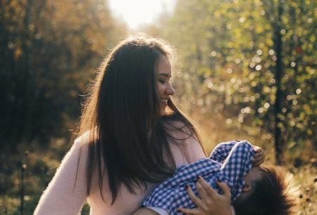 Joyful mother holding hands and spinning her son in the forest. Happy boy having fun with his mother.の写真素材