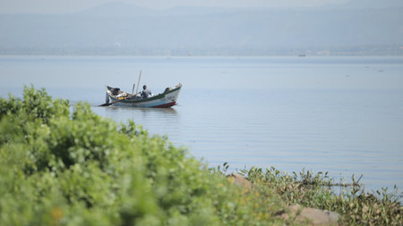KENYA, KISUMU - MAY 20, 2017: African man sitting in the boat and rowing alone. Fisherman is working in the sea.のeditorial素材