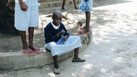 KENYA, KISUMU - MAY 20, 2017: Bald african girl sitting outside near the school and looking inside the bag, open present.のeditorial素材