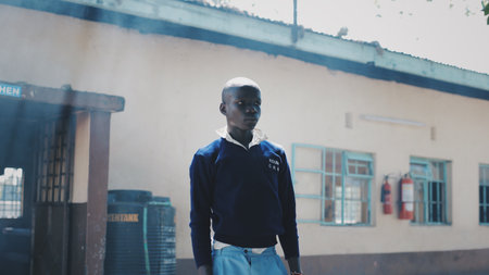 KENYA, KISUMU - MAY 20, 2017: African boy in uniform clapping hands and dancing outside. The bald male is singing along.のeditorial素材
