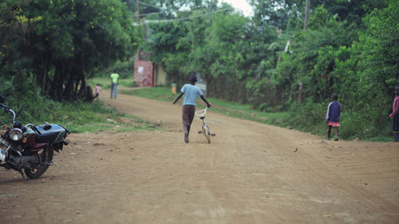 KENYA, KISUMU - MAY 20, 2017: Back view of boy walking through the road in Africa. Male with bicycle walking in forest.のeditorial素材