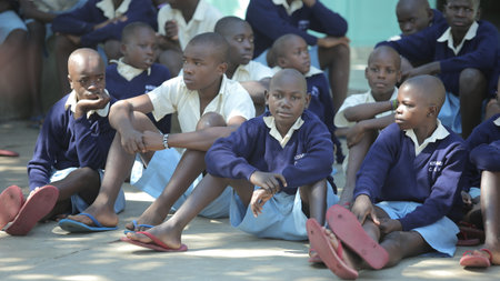 KENYA, KISUMU - MAY 20, 2017: Group of african children sitting on ground. Boys and girls in uniform spend time outside. Handsome boy smiling Ð°n the cameraのeditorial素材