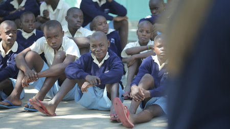 KENYA, KISUMU - MAY 20, 2017: Group of african children sitting on ground. Boys and girls in uniform spend time outside. Handsome boy smiling Ð°n the cameraのeditorial素材