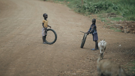 KENYA, KISUMU - MAY 20, 2017: Two african boys playing with tires on the road. Kids having fun togetherのeditorial素材