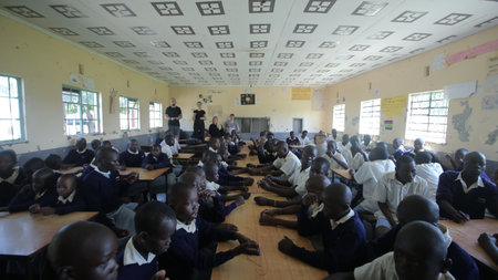 KENYA, KISUMU - MAY 23, 2017: Big group of african kids and teenagers sitting, caucasian volunteers help make braceletsのeditorial素材