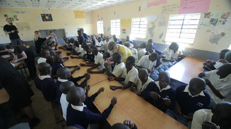 KENYA, KISUMU - MAY 23, 2017: Big group of african kids and teenagers sitting, caucasian volunteers help make braceletsのeditorial素材