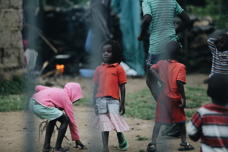 KENYA, KISUMU - MAY 20, 2017: View through the fence. Group of african people spending time outside. Little girl having fun.のeditorial素材