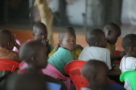 KENYA, KISUMU - MAY 23, 2017: Portrait of happy african boy sitting inside with group of children and dancing, smiling.のeditorial素材