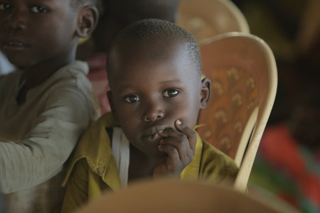 KENYA, KISUMU - MAY 23, 2017: Portrait of happy african boy sitting inside with group of children and dancing, smiling.のeditorial素材