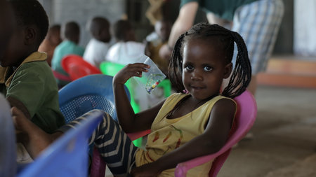 KENYA, KISUMU - MAY 23, 2017: Portrait of happy african girl sitting inside with group of children and dancing, smiling.のeditorial素材