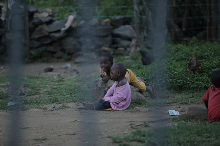 KENYA, KISUMU - MAY 23, 2017: View through the fence. Group of african people spending time outside. Little kids having fun.のeditorial素材