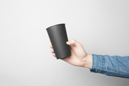 Hand in blue shirt is holding a black paper cupの写真素材