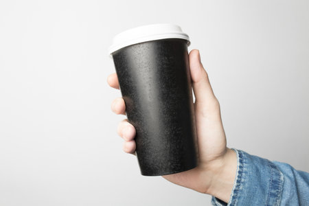 Hand in blue shirt is holding a black paper cupの写真素材
