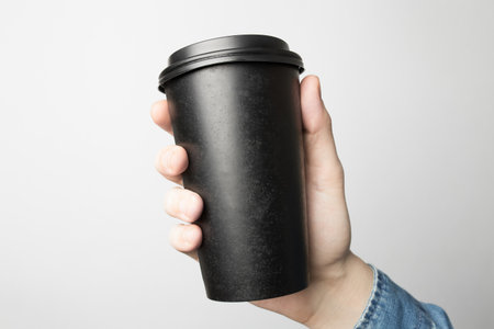 Hand in blue shirt is holding a black paper cupの写真素材