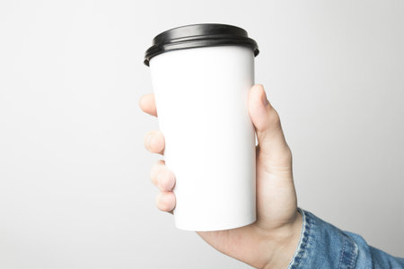 Hand in blue shirt is holding a white paper cupの写真素材