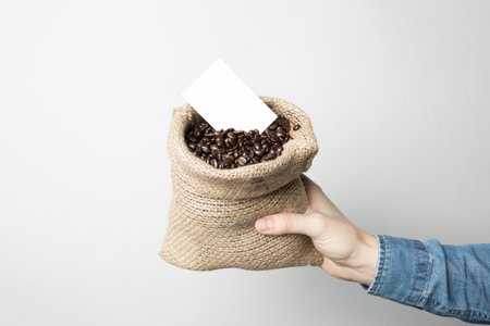 Hand in blue shirt is holding a coffee sack with business cardの写真素材