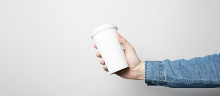 Hand in blue shirt is holding a white paper cupの写真素材