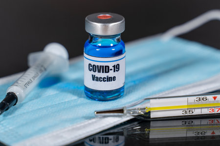 Close up of COVID 19 vaccine vial, syringe, face mask and thermometer.の写真素材