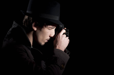 Private detective taking pictures with a small camera, isolated in black