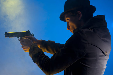 Man holding a gun, shooted in studio on a blue background with yellow light and smokeの写真素材