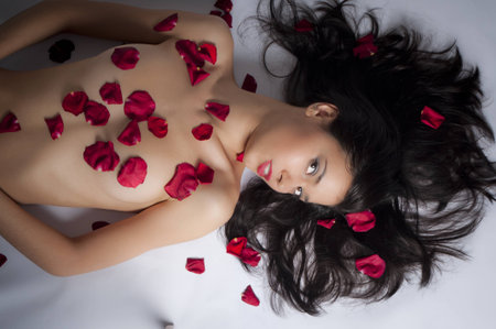 beautiful suntanned female body in petals of scarlet rosesの写真素材