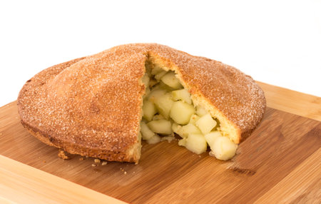 Homemade apple pie with slice removed covered in sugar on wooden chopping board