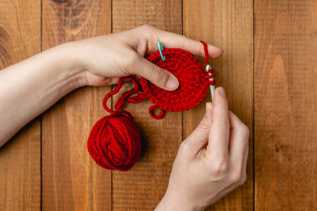 Womens hands knit on the spokes a pattern of soft acrylic yarn of red color. Knitting, hobby and...