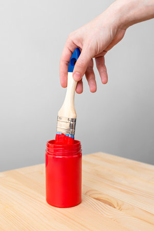 A girl's hand with a brush with red paint over a can of paint.の写真素材