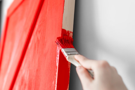 A girl paints the barn door. The hand holds a brush with red paint. Surface painting.の写真素材