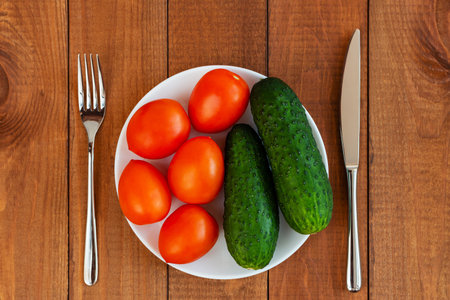 Cucumbers and tomatoes on a white plate. A plate with vegetables on the table. diet food. Vegetarian food.の写真素材