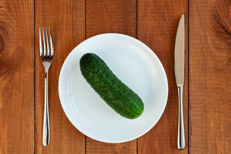 Green cucumber on a white plate. A plate with vegetables on the table. Diet food. Vegetarian food.の写真素材
